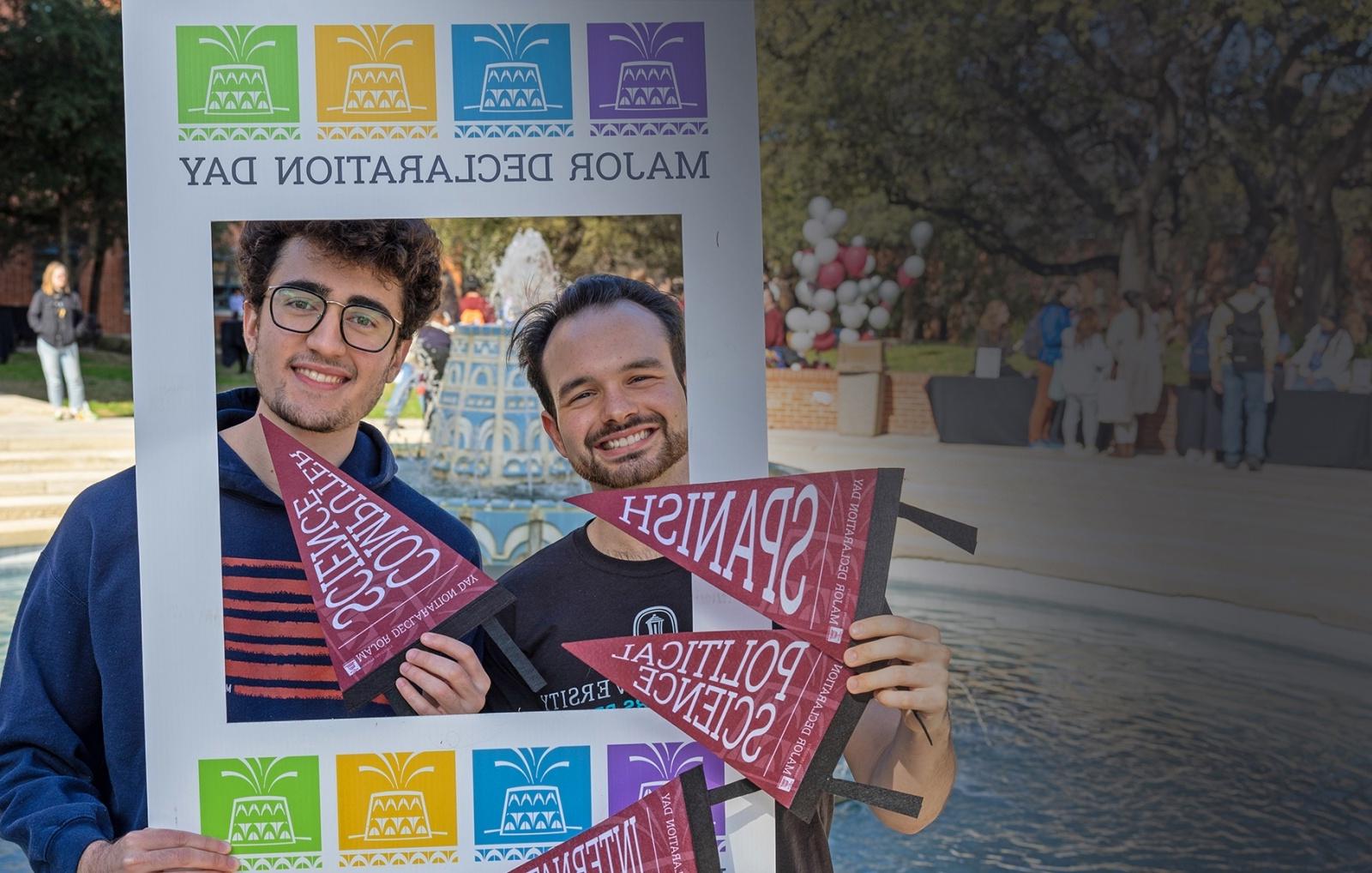 Blaine Martin 和 Caleb Aguiar pose in front of the fountain with a 主要 Declaration Day frame